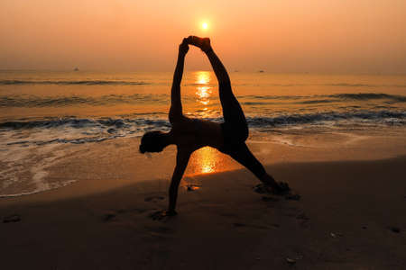 Silhouette young woman practicing yoga on the beach at sunriseの写真素材