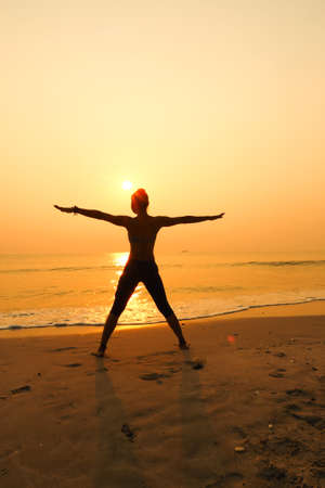 Silhouette young woman practicing yoga on the beach at sunriseの写真素材