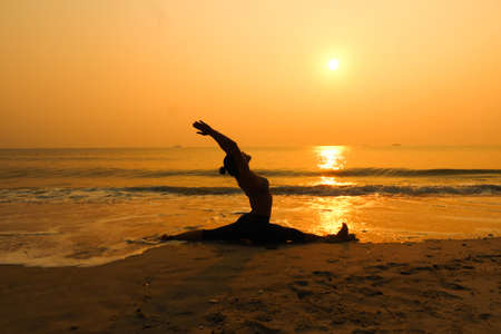Silhouette young woman practicing yoga on the beach at sunriseの写真素材