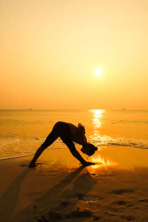 Silhouette young woman practicing yoga on the beach at sunriseの写真素材