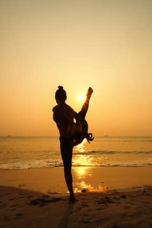 Silhouette young woman practicing yoga on the beach at sunriseの写真素材
