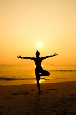 Silhouette young woman practicing yoga on the beach at sunriseの写真素材