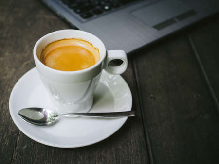 cup of coffee latte on the wood texture with laptop computer in vintage color toneの写真素材