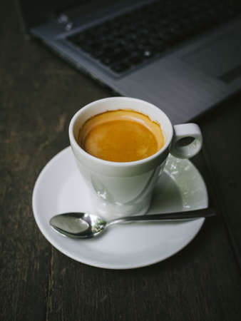 cup of coffee latte on the wood texture with laptop computer in vintage color toneの写真素材