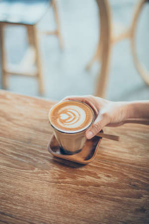 woman hand with cup of coffee latte art on the wood desk in vintage color toneの写真素材