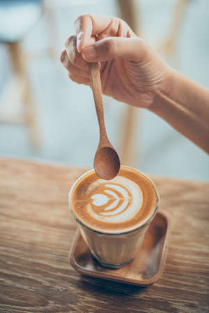 woman hand with cup of coffee latte art on the wood desk in vintage color toneの写真素材