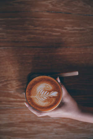 Woman hand hold cup of coffee latte on the wood texture   in vintage color toneの写真素材