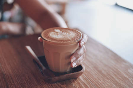 Woman hand hold cup of coffee latte on the wood texture   in vintage color toneの写真素材