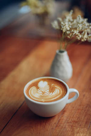 cup of coffee latte art on the wooden desk in coffee shop cafe with vintage color tone filter backgroundの写真素材