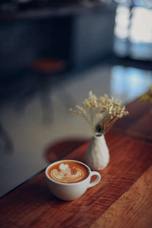 cup of coffee latte art on the wooden desk in coffee shop cafe with vintage color tone filter backgroundの写真素材