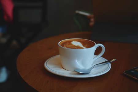 cup of coffee latte art on the wooden desk in coffee shop cafe with vintage color tone filter backgroundの写真素材