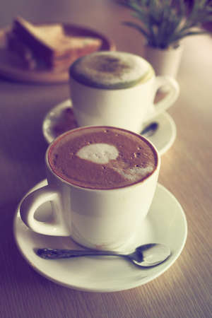 cup of coffee latte art on the wooden desk in coffee shop cafe with vintage color tone filter backgroundの写真素材