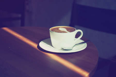cup of coffee latte art on the wooden desk in coffee shop cafe with vintage color tone filter backgroundの写真素材