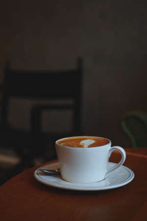 cup of coffee latte art on the wooden desk in coffee shop cafe with vintage color tone filter backgroundの写真素材