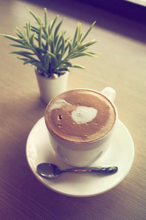 cup of coffee latte art on the wooden desk in coffee shop cafe with vintage color tone filter backgroundの写真素材