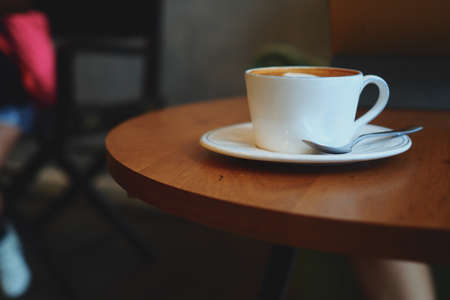 cup of coffee latte art on the wooden desk in coffee shop cafe with vintage color tone filter backgroundの写真素材