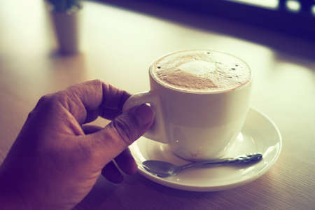 cup of coffee latte art on the wooden desk in coffee shop cafe with vintage color tone filter backgroundの写真素材