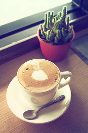 cup of coffee latte art on the wooden desk in coffee shop cafe with vintage color tone filter backgroundの写真素材