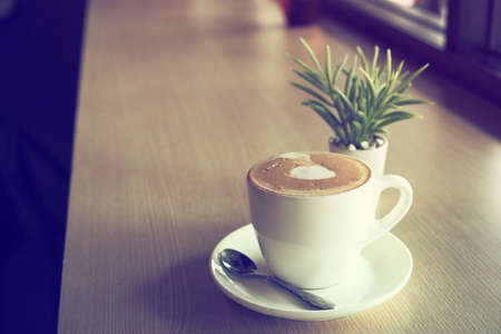 cup of coffee latte art on the wooden desk in coffee shop cafe with vintage color tone filter backgroundの写真素材