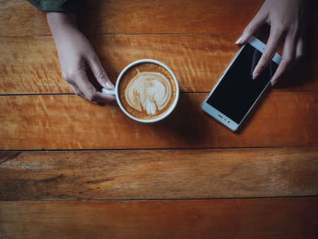 coffee latte art in coffee shop wood texture background with woman hand in vintage color toneの写真素材