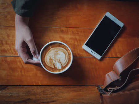 coffee latte art in coffee shop wood texture background with woman hand in vintage color toneの写真素材