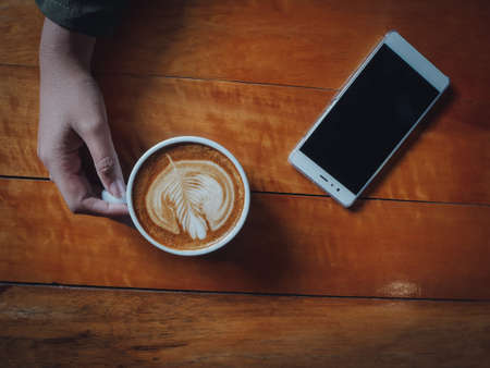 coffee latte art in coffee shop wood texture background with woman hand in vintage color toneの写真素材