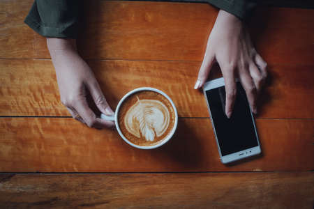 coffee latte art in coffee shop wood texture background with woman hand in vintage color toneの写真素材