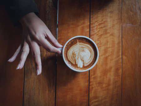 coffee latte art in coffee shop wood texture background with woman hand in vintage color toneの写真素材