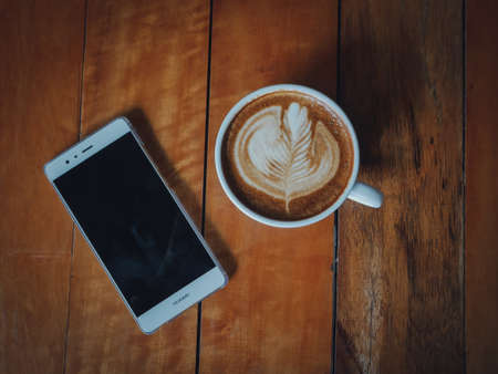 coffee latte art in coffee shop wood texture background with woman hand in vintage color toneの写真素材