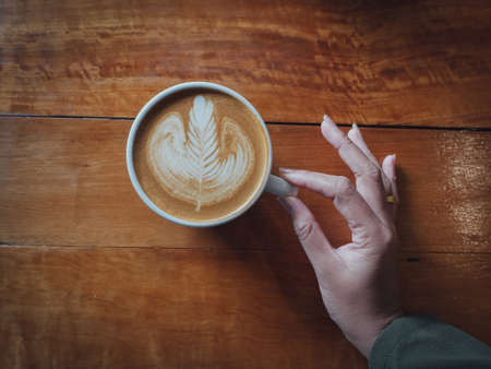 coffee latte art in coffee shop wood texture background with woman hand in vintage color toneの写真素材