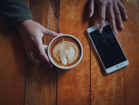coffee latte art in coffee shop wood texture background with woman hand in vintage color toneの写真素材