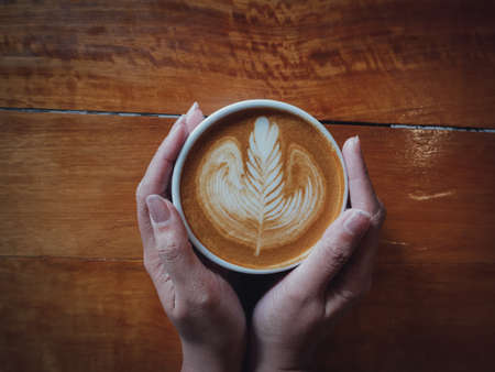 coffee latte art in coffee shop wood texture background with woman hand in vintage color toneの写真素材