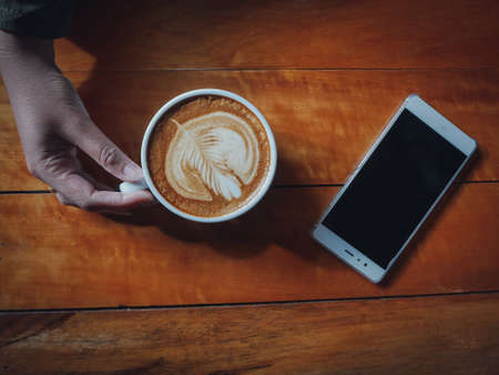 coffee latte art in coffee shop wood texture background with woman hand in vintage color toneの写真素材