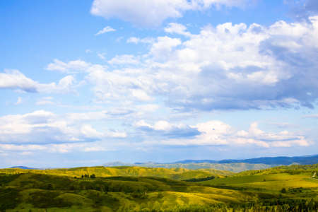 Hills with green grass and blue sky with white puffy cloudsの写真素材