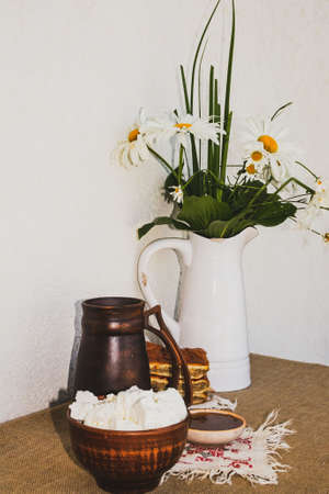 Homemade cottage cheese, honey, pie, a jug of milk and a jug with a bouquet of chamomiles.の写真素材
