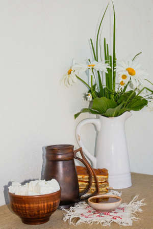 Homemade cottage cheese, honey, pie, a jug of milk and a jug with a bouquet of chamomiles.の写真素材