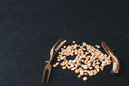 Peas and decorative fork and knife on a dark background.