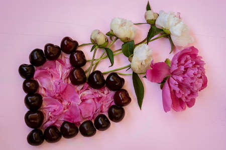 Bouquet of flowers and heart shape from cherry berries and peony petals on a pink wooden background.の写真素材