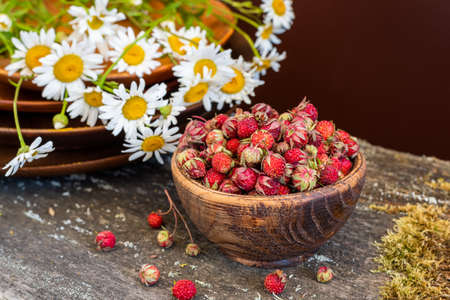 Sweet forest strawberries and a bouquet of daisies on a wooden backgroundの写真素材