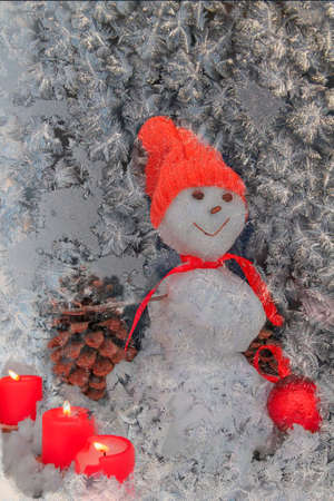 Christmas snowman looks through a frozen glass with hoarfrost.の写真素材