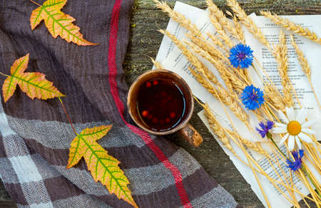 Autumn still life with a cup of tea, ears of wheat, cornflowers, a warming scarf and colorful leaves