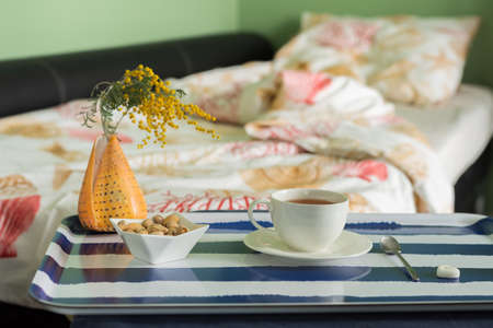 Unmade bed with a sea pattern and a table with a cup of tea and a seashell.