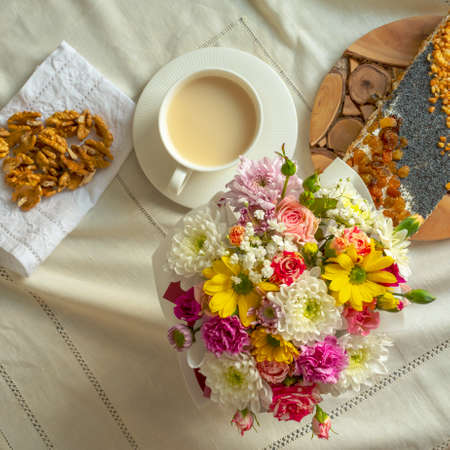 Breakfast at a table with a white tablecloth - a cup, sweet cake, walnuts and a bouquet of flowersの写真素材