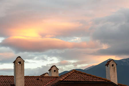 Clouds in the rays of the setting sun against the background of the tiled roofの写真素材