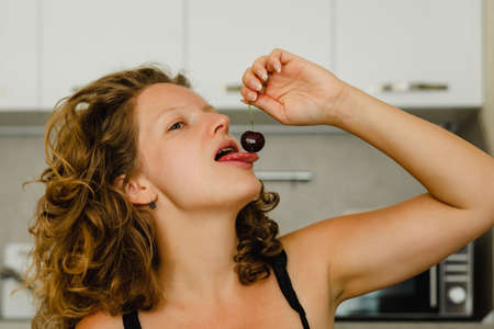 Young woman eating cherry berry in the kitchenの写真素材