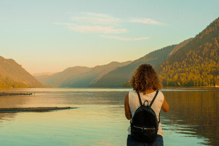 Young woman sits on the shore of the lake in the evening.の写真素材