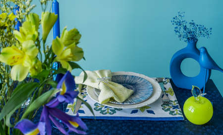 Table setting in blue and yellow colors. On a dark tablecloth a plate, a vase of flowers and decorの写真素材