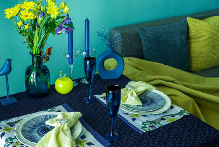 Table setting for two in blue and yellow colors against the background of a sofa with pillows.の写真素材