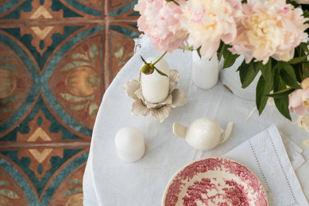 Table setting with a cup of tea and white peonies in a white ceramic jugの写真素材
