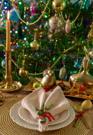 New Years table setting in gold color, against the background of a decorated Christmas tree.の写真素材